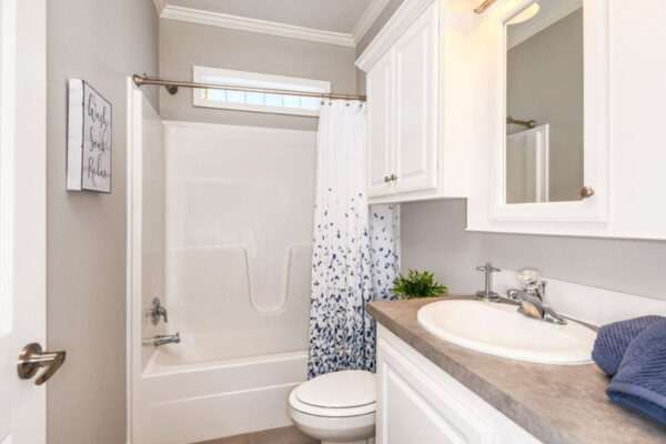 Hall bathroom with a 60" tub/shower, white cabinets, a medicine cabinet over the sink and linen over the toilet